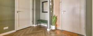 Ingresso di casa arredato con panca verde, specchio a parete e pianta decorativa vicino alla porta d’ingresso.