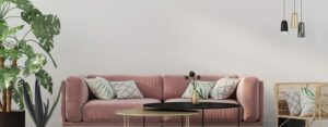 Divano rosa in un salotto moderno con tavolini, cuscini decorativi, piante verdi e lampade sospese.